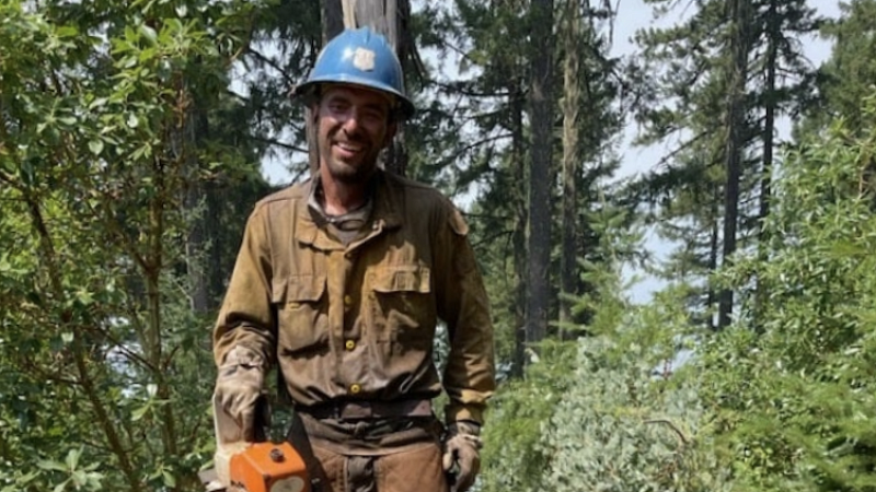 Forestry worker smiling and holding a chainsaw after cutting down a tree in the woods.
